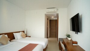 A hotel room with two beds, a desk, a chair, a TV, and an air conditioning unit. - THE LEDGE ULUWATU (Pecatu)