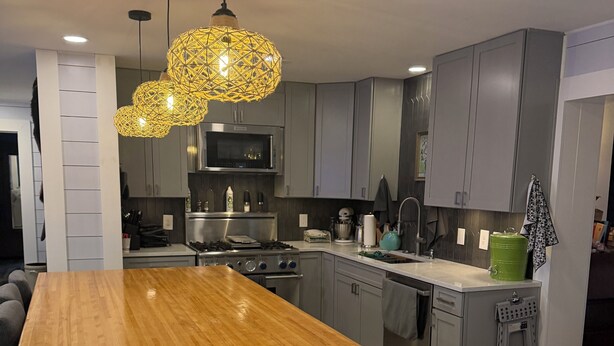 Cozinha moderna com ilha de madeira, armários cinzas, eletrodomésticos de aço inoxidável e uma luminária pendente amarela marcante.