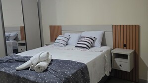 A neatly made bed with a polka dot blanket and rolled towels, a bedside nightstand, a mirror, and an air conditioning unit on the wall. - Luxury apartment 200 meters from the beach. (Porto Seguro)