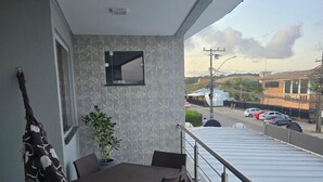 A balcony with a table and chairs, a patterned sofa, a potted plant, and a view of a street with parked cars and buildings. - Luxury apartment 200 meters from the beach. (Porto Seguro)