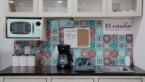 Une cuisine équipée d’un four à micro-ondes, d’une machine à café et d’un tableau d’affichage en liège sur lequel est affiché un message de bienvenue.