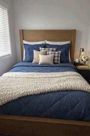 Un lit avec une couette bleue, un jeté blanc et des coussins à carreaux.