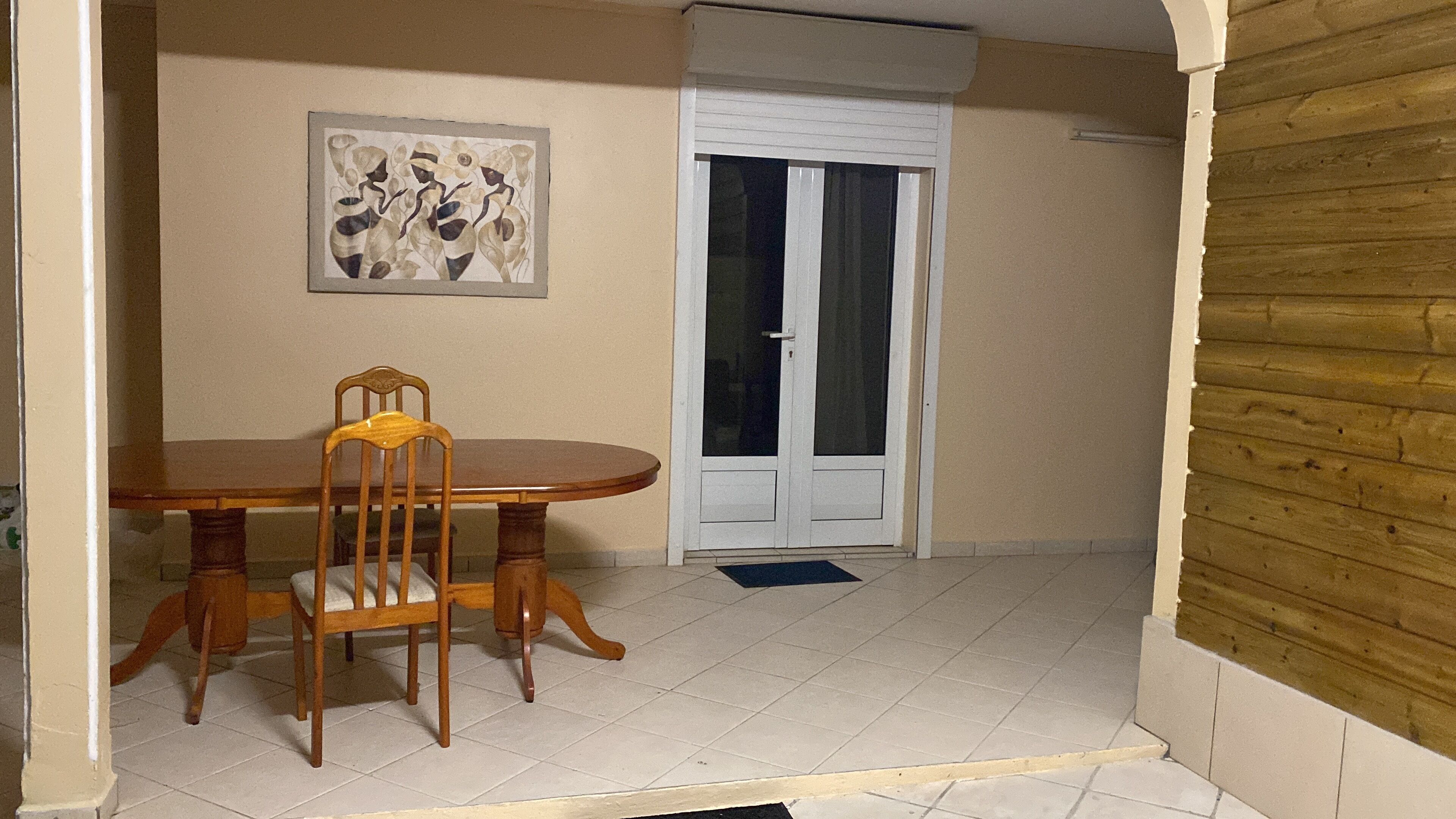 A dining area with a wooden table and chairs, a door with glass panels, and a wall-mounted artwork.