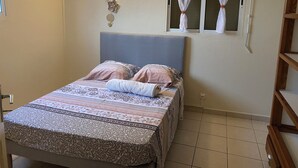 Un dormitori amb un llit, una finestra amb cortines transparents, un aparell d'aire condicionat i una làmpada fixa a la paret.