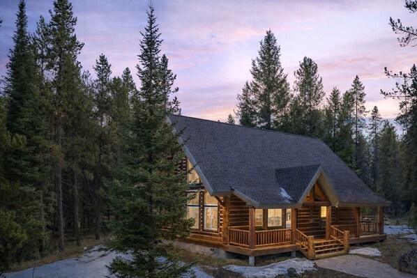 A log cabin with a porch, surrounded by dense forest.