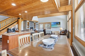 A spacious kitchen with a stone fireplace, wooden ceiling, and a dining area with a large table and chairs.