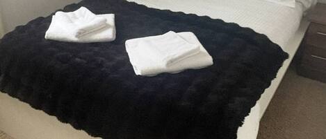 Een bed met een zwart deken en twee opgevouwen witte handdoeken, een bedlamp en een nachtkastje.