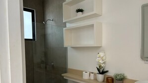 A modern bathroom with a glass shower enclosure, a toilet, a sink, and built-in shelves with toiletries. - Modern studio in Tamarindo forest (Tamarindo)