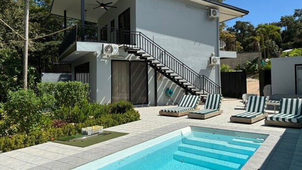 Ett modernt hus i två våningar med pool, utomhusmöbler och en trappa som leder upp till övre våningen.