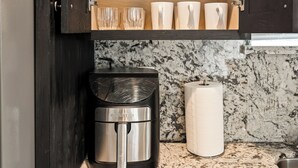 Cuina amb cafetera integrada, taulell de marbre i una estant amb glops de vi i tasses.