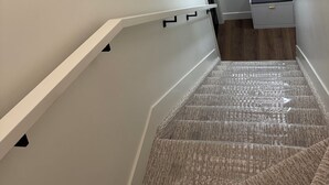 Una escalera con alfombra texturizada, paredes blancas y decoración mural ornamental.