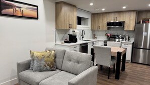 Una cocina moderna con armarios de madera, un refrigerador de acero inoxidable y una zona de comedor con sofá y sillas grises.