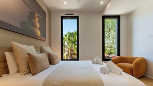 A bedroom with a bed, pillows, a blanket, a painting, and two windows. - 2 Villas • Beach • Pools • Large groups (Agde)