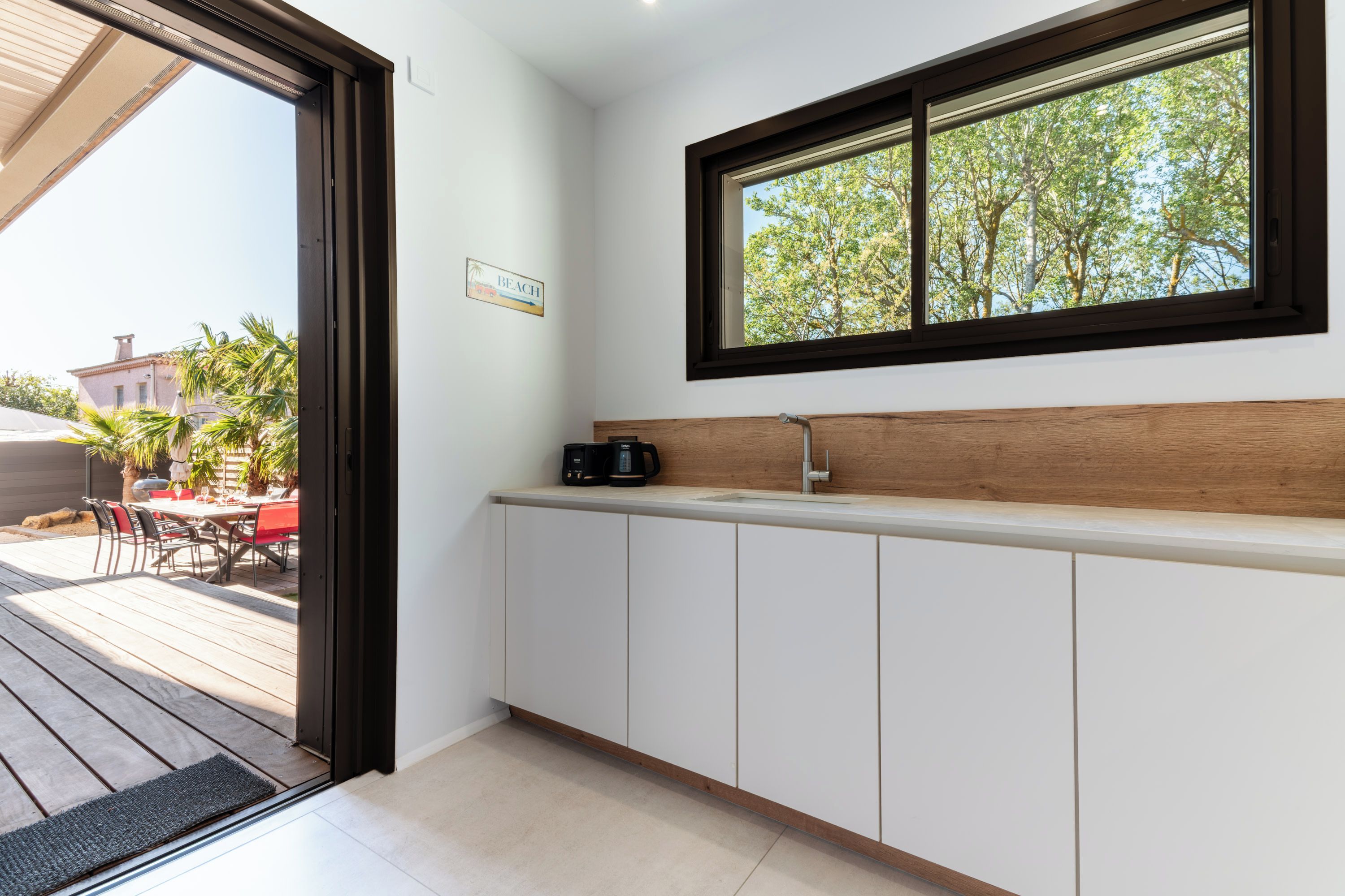 Een moderne keuken met een houten aanrecht, een raam met uitzicht op bomen, en een deur naar een terras.
