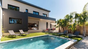 A modern house with a swimming pool, outdoor seating, and a well-maintained lawn. - 2 Villas • Beach • Pools • Large groups (Agde)