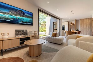 A modern living room with a large flat-screen TV, a dining area, and a view of the outdoors. - 2 Villas • Beach • Pools • Large groups (Agde)