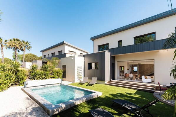 Ein modernes Haus mit Swimmingpool, Terrasse mit Stühlen und einem gepflegten Rasen.