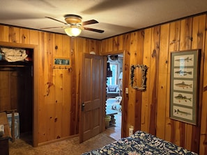 Ein Zimmer mit Holzwandverkleidung, einem Deckenventilator, einer Tür zu einer Veranda und einem gerahmten Bild mit einem Fisch.