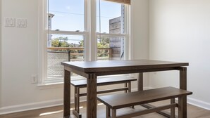 Una habitación con una mesa y banco de madera, una ventana con persianas y vista a una zona residencial.