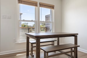 Una habitación con una mesa y banco de madera, una ventana con persianas y vista a una zona residencial.