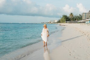 A beach with a person walking along the shore, a clear sky, and distant buildings. - Luxury Grace Bay Villa 2/private pool/2 min walk to reef&beach (The Bight Settlement)