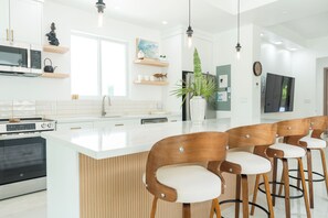 A modern kitchen with a central island, bar stools, a microwave, and a refrigerator. - Luxury Grace Bay Villa 2/private pool/2 min walk to reef&beach (The Bight Settlement)