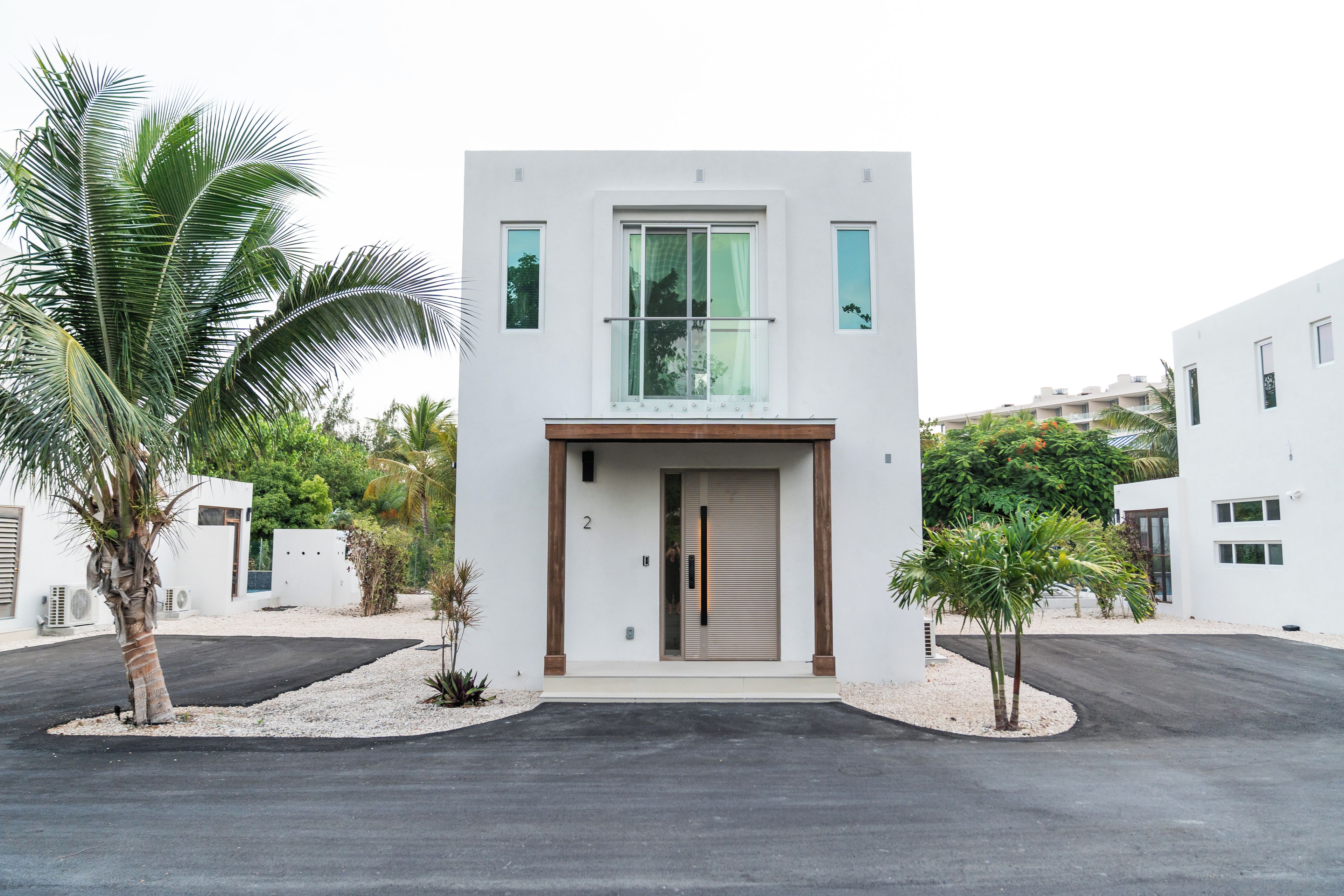 A modern two-story building with a flat roof, a central entrance with a glass door, and a small balcony.