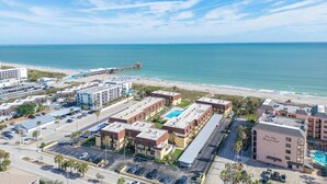 Vista aérea de uma área de hotel à beira-mar, com praia, estacionamentos e um edifício grande com piscina.