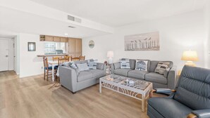 Uma sala de estar moderna com um sofá cinzento, uma mesa de centro e um espaço de refeições com cadeiras de madeira.