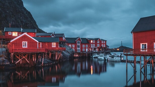 En havnefront med røde bygninger, heriblandt et museum, og både fortøjet i stille vand.