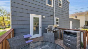A deck with a grill, a glass table, and chairs. - Great Home_Comfy Beds_Sleeps 8_Hot Tub & Game Room (Kansas City)