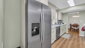 A modern kitchen with a stainless steel refrigerator, white cabinets, a built-in water dispenser, and a dining area with a table and chairs. - Great Home_Comfy Beds_Sleeps 8_Hot Tub & Game Room (Kansas City)
