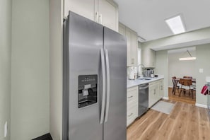 Eine moderne Küche mit einem Edelstahl-Kühlschrank, weißen Schränken, einem integrierten Wasserspender und einem Essbereich mit Tisch und Stühlen.
