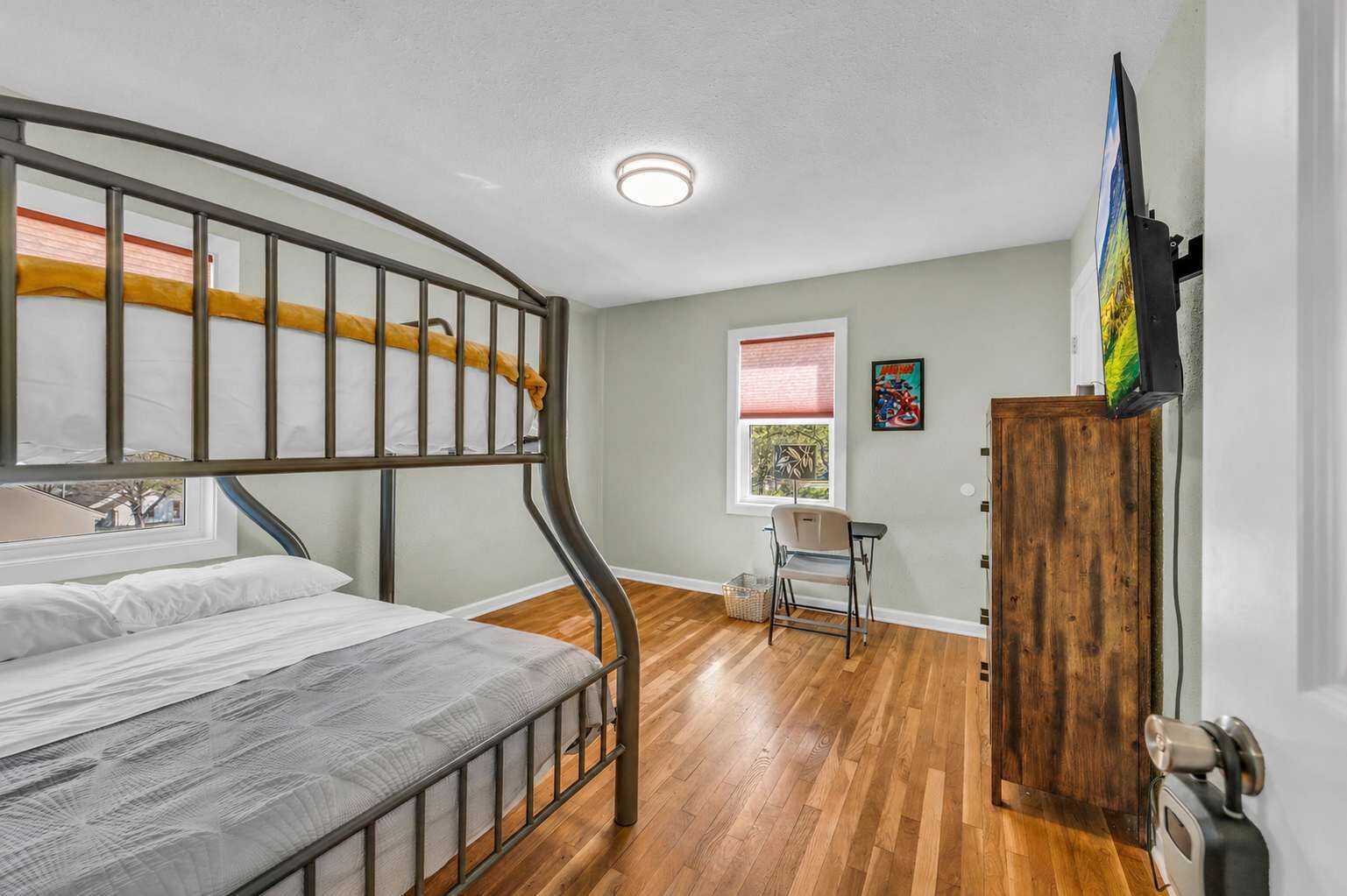 A bunk bed room with a desk, a chair, a window, and a television.