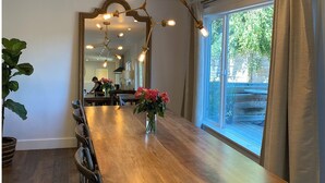 Uma sala de jantar com uma longa mesa de madeira, cadeiras, um vaso de flores e um candelabro.