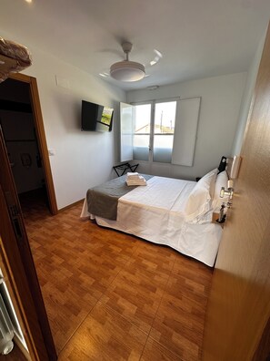 A bedroom with a bed, a ceiling fan, a TV mounted on the wall, and a window with a view. - Pensión Mirador de Rourís (O Pino)
