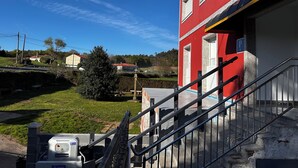 A red building with a staircase leading to a door, a parking sign, and a clear blue sky. - Pensión Mirador de Rourís (O Pino)