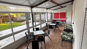 A covered outdoor seating area with tables and chairs, a red wall, and a view of a garden. - Pensión Mirador de Rourís (O Pino)