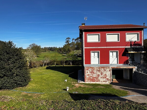 A red building with a garage, surrounded by a well-maintained lawn and trees. - Pensión Mirador de Rourís (O Pino)