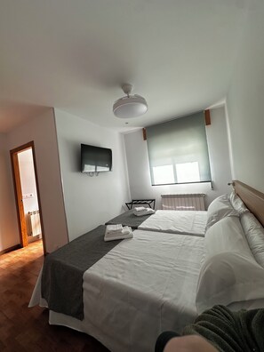 A hotel room with a bed, a TV mounted on the wall, a window with blinds, and a ceiling fan. - Pensión Mirador de Rourís (O Pino)