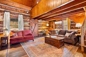 A log cabin interior with a red sofa, a brown sofa, a wooden coffee table, and a patterned rug.