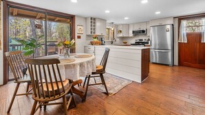 Una cocina moderna con armarios blancos, un refrigerador de acero inoxidable y un comedor con sillas de madera y una mesa redonda.