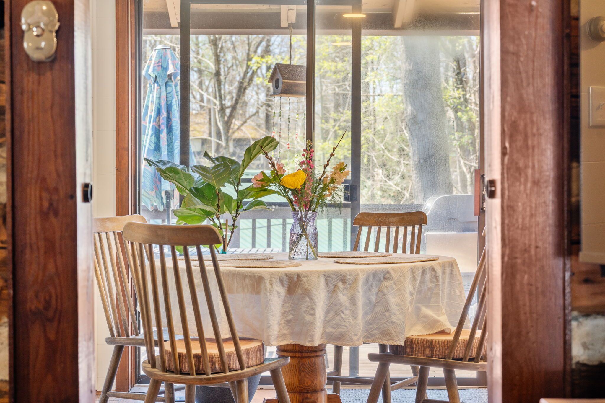 A dining area with a round table, four wooden chairs, and a vase with flowers.