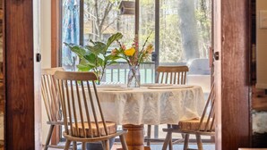 Un comedor con una mesa redonda, cuatro sillas de madera y un jarrón con flores.