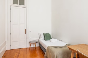 Ein kleines, aufgeräumtes Schlafzimmer mit einem Einzelbett, einem Nachttisch, einem kleinen Hocker und einer Tür mit Milchglasfenster.