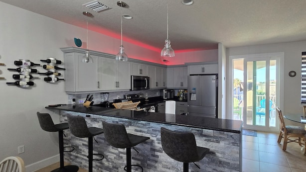 Una cocina moderna con una isla central, taburetes de bar y un comedor con sillas de mimbre.