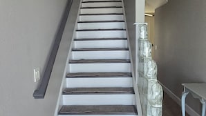 Una escalera con barandilla, un rellano alfombrado y un banco.