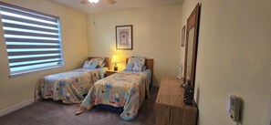 Une chambre avec deux lits, une table de chevet, une lampe, un tableau encadré et un miroir.