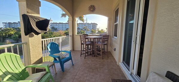 A balcony with a table and chairs, a blue chair, a green chair, and a hanging towel.