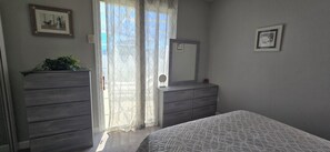 A bedroom with a bed, two dressers, a mirror, and a window with curtains.